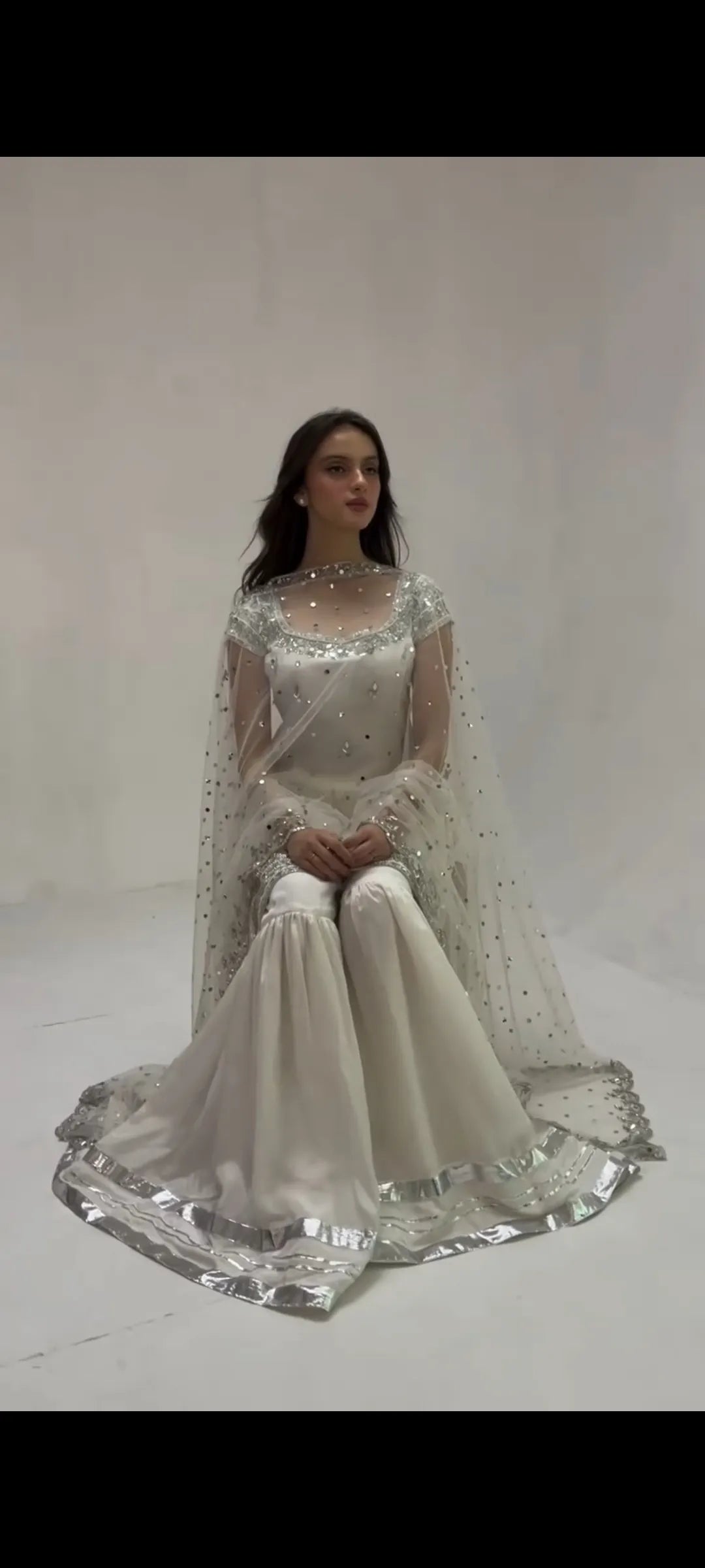 Woman wearing a white embroidered traditional outfit on a plain background